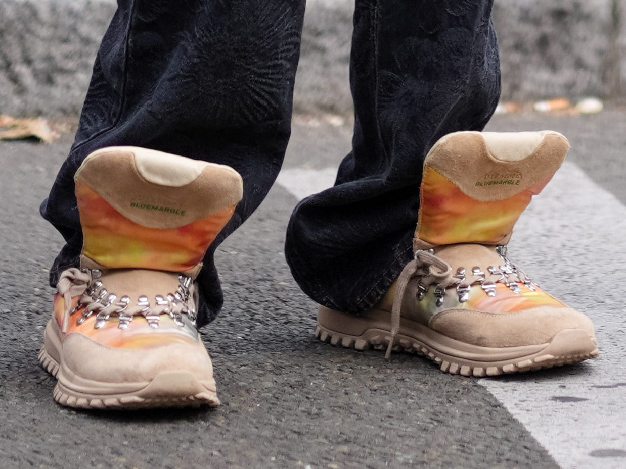 A man wearing black pants and sneakers with an oversize tongue.