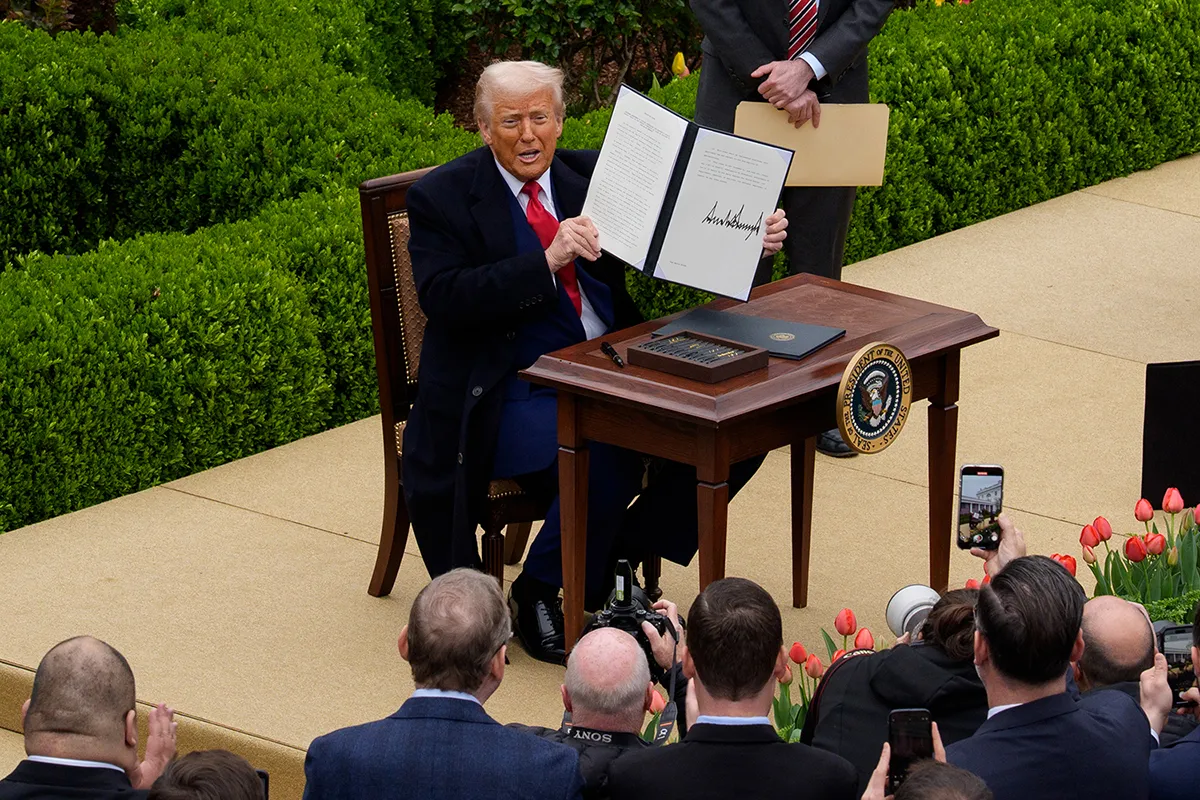 Donald Trump holds up a signed executive order at a desk.