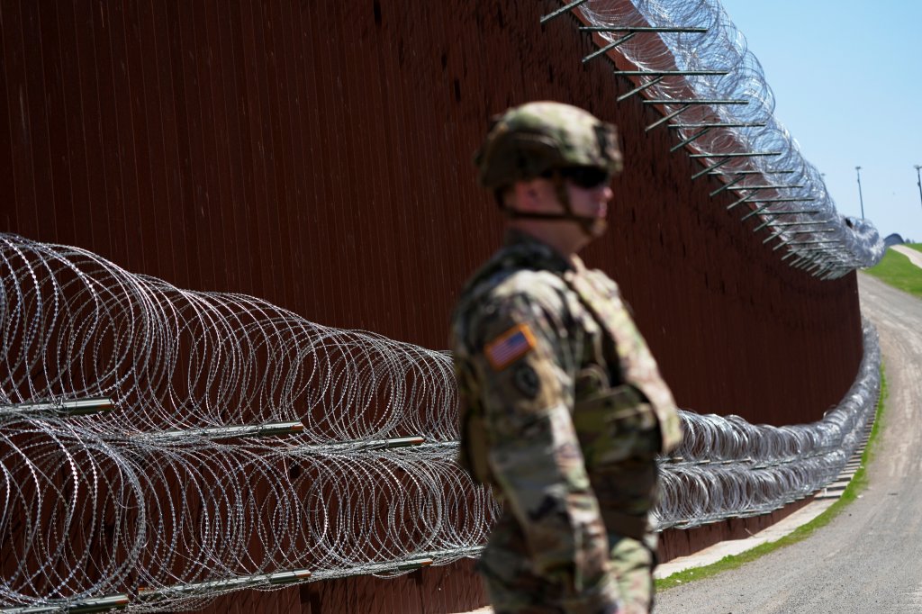 US soldier standing near border wall with razor wire.