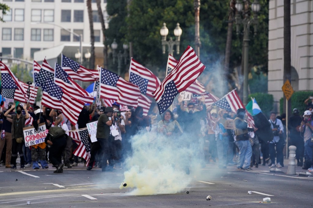 Demonstrators hold U.S. flags and signs amid tear gas during a protest against U.S. President Donald Trump's policies and federal immigration sweeps.