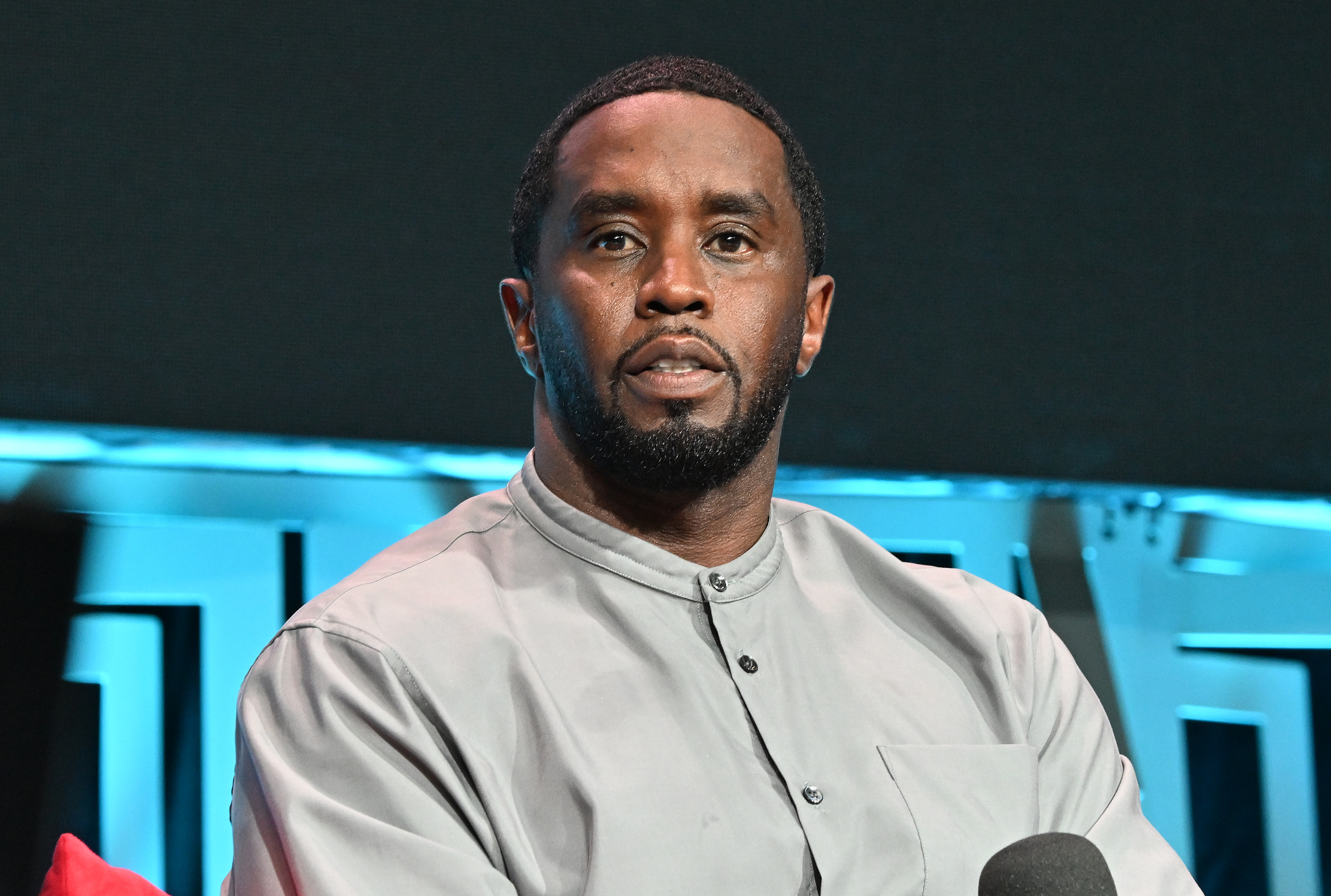Sean Combs sits in a beige shirt. 