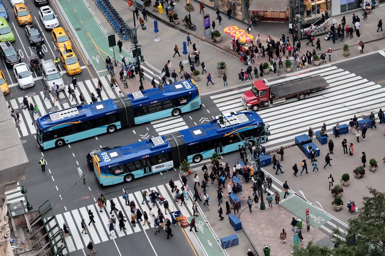 Two MTA buses pass through Herald Square on 34th Street in New York City.