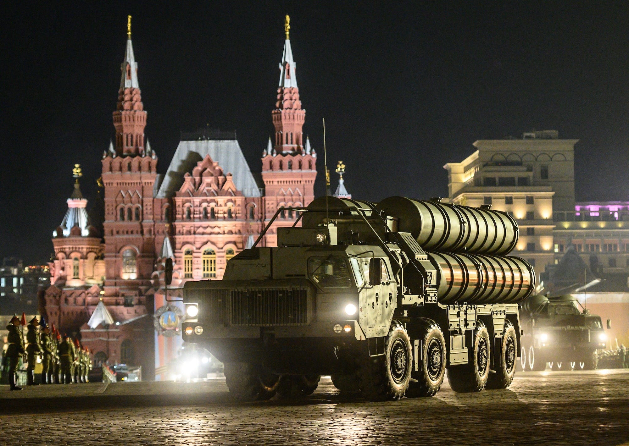 A piece of weaponry made up of large green cylinders on the back of a truck on a street at nighttime in front of a red building