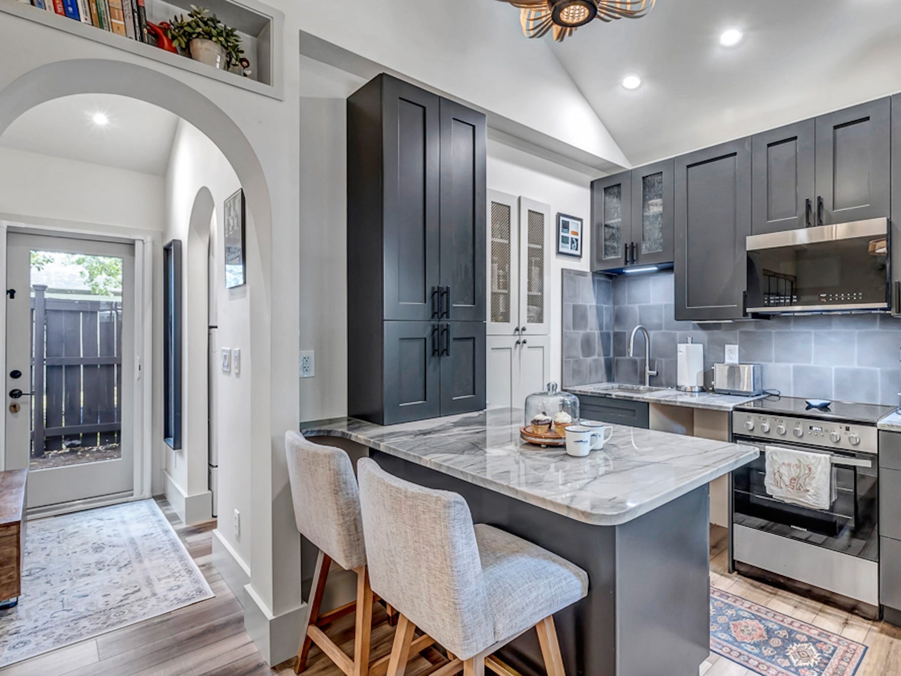 A photo of a kitchen with gray cabinetry and an entryway with an archway leading to it.