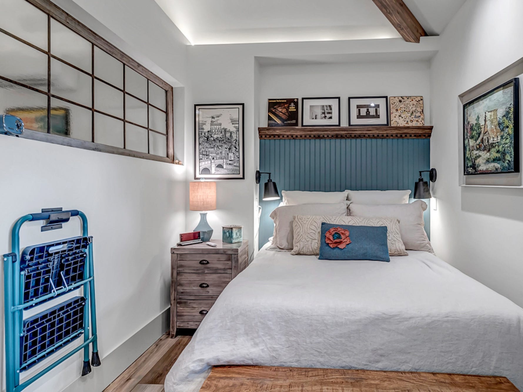 A small bedroom with a window and and a bed with a blue headboard.