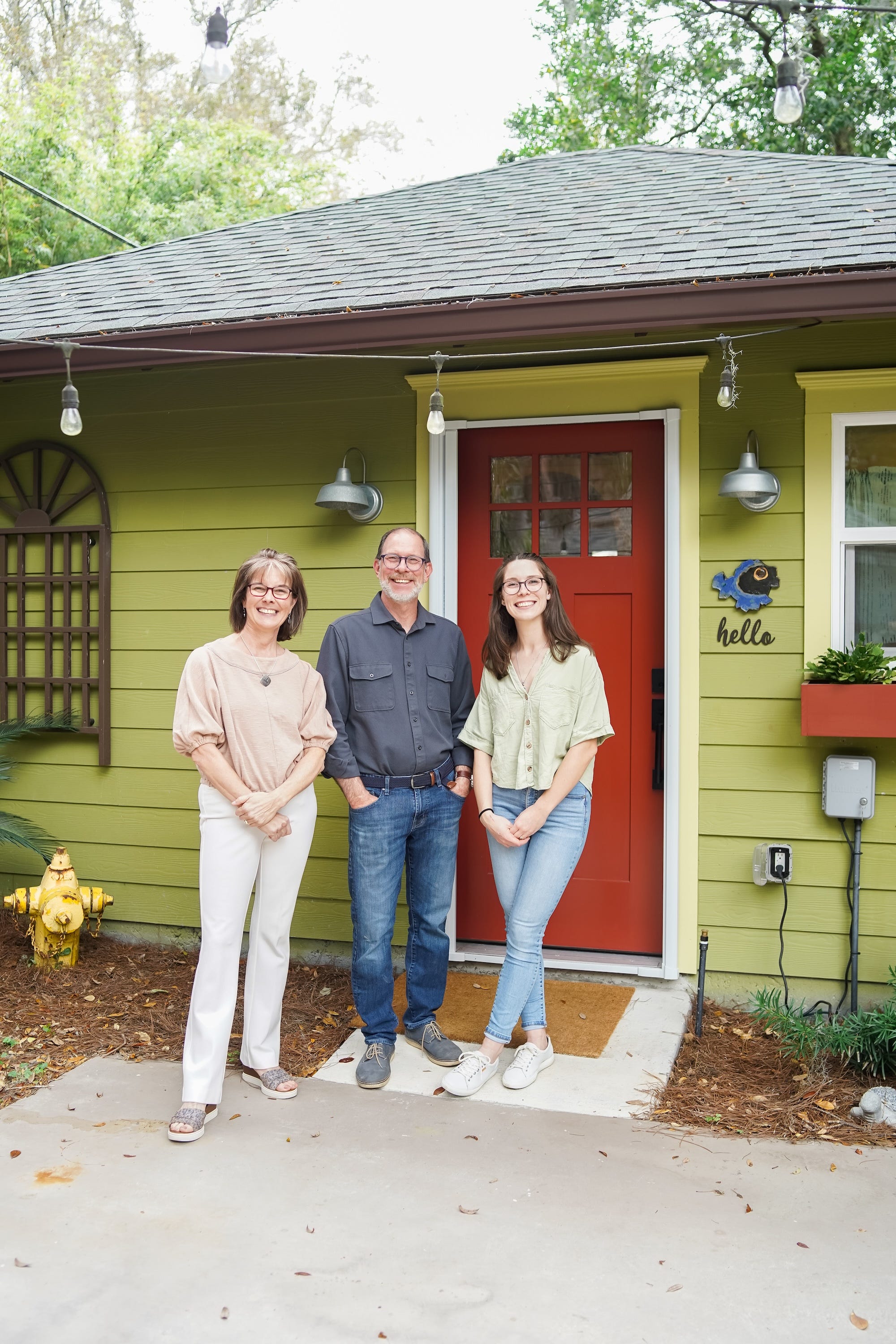 A photo of three people in front of a green apartment with a red door.