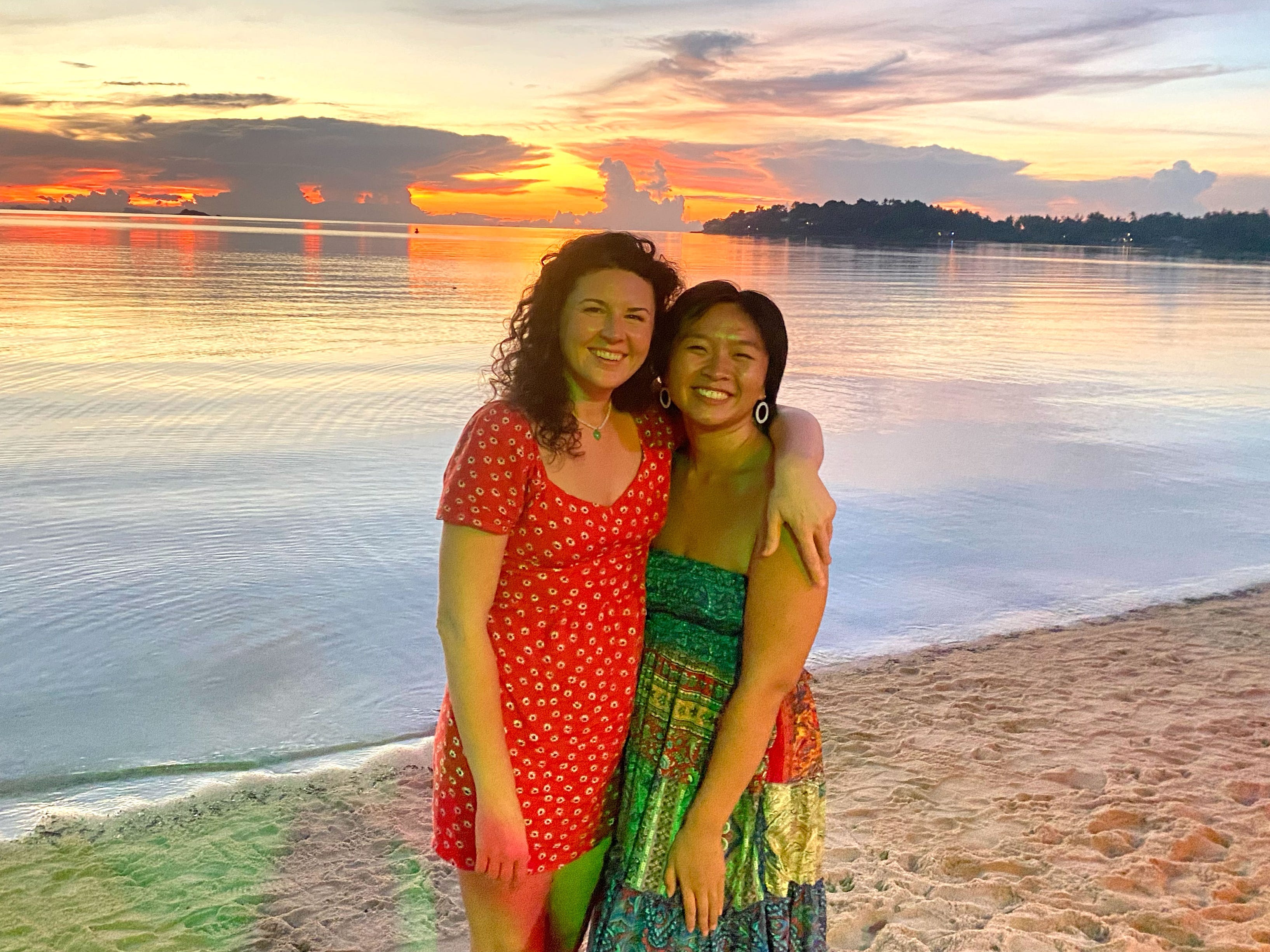 Christina and a friend pose on a beach in Thailand at sunset.