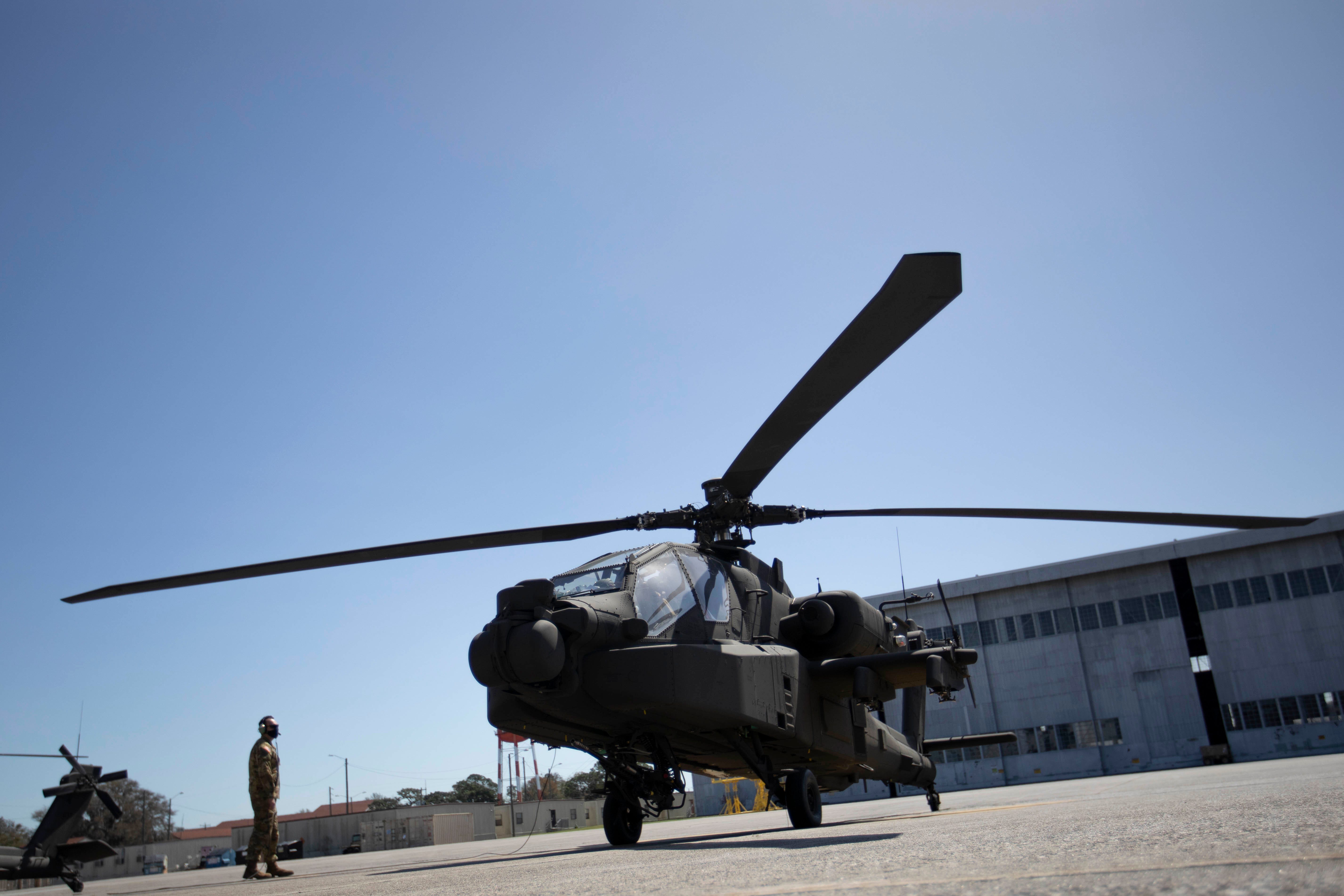 A black helicopter is seen from a low angle on a tarmac with a blue sky in the background.