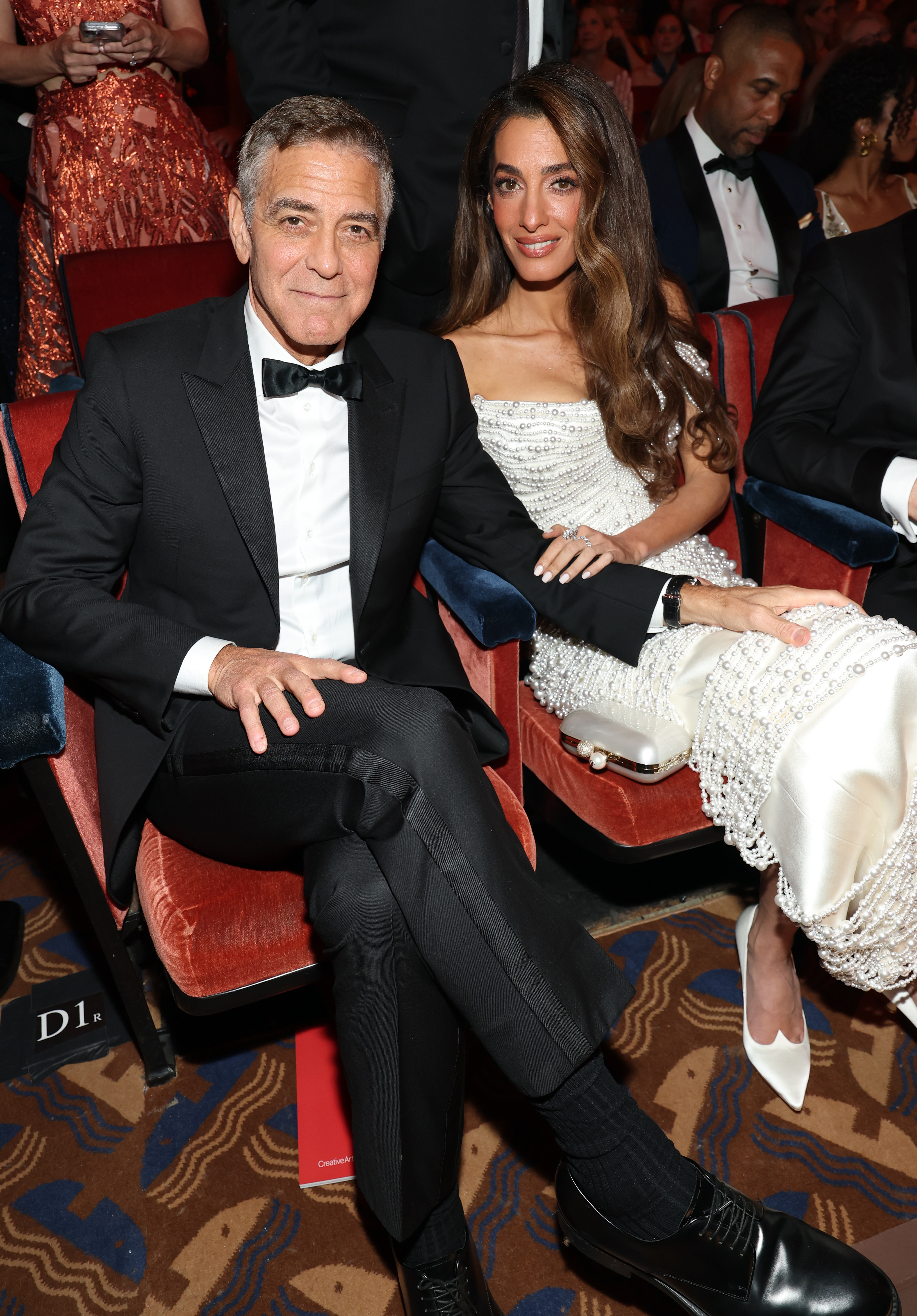 Amal and George Clooney sit at a formal event. 