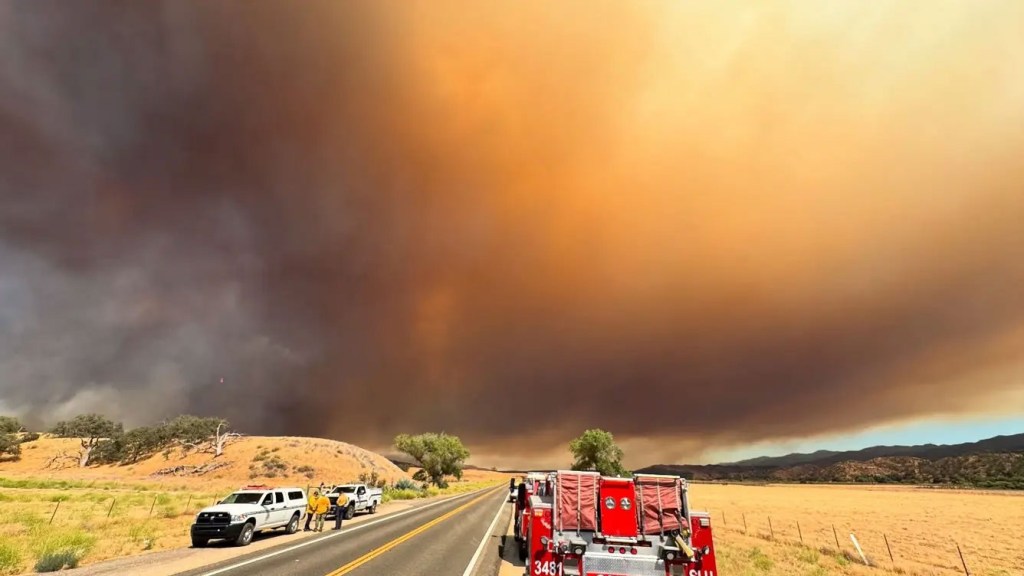 Firefighters and vehicles near a large wildfire.