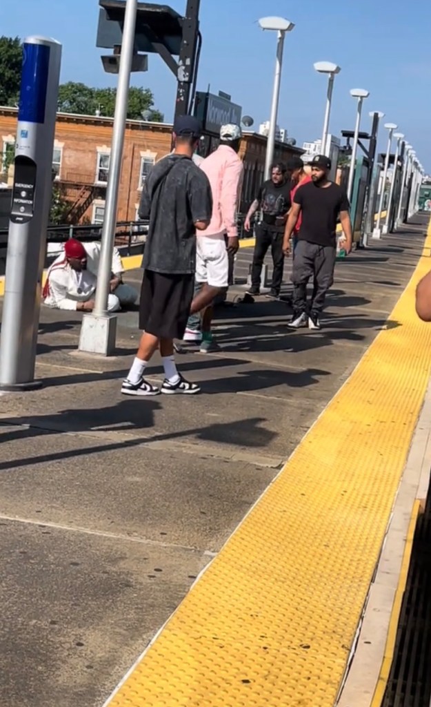 People standing on a subway platform, one person is sitting on the ground.