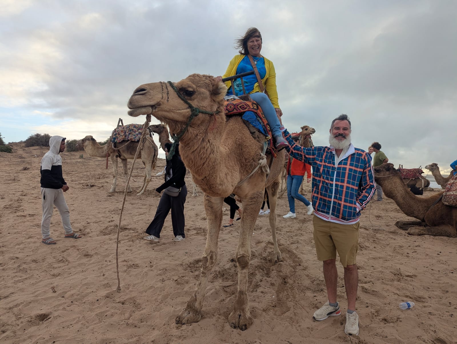 The author's husband smiling while standing next to his mother, who is sitting on a camel.