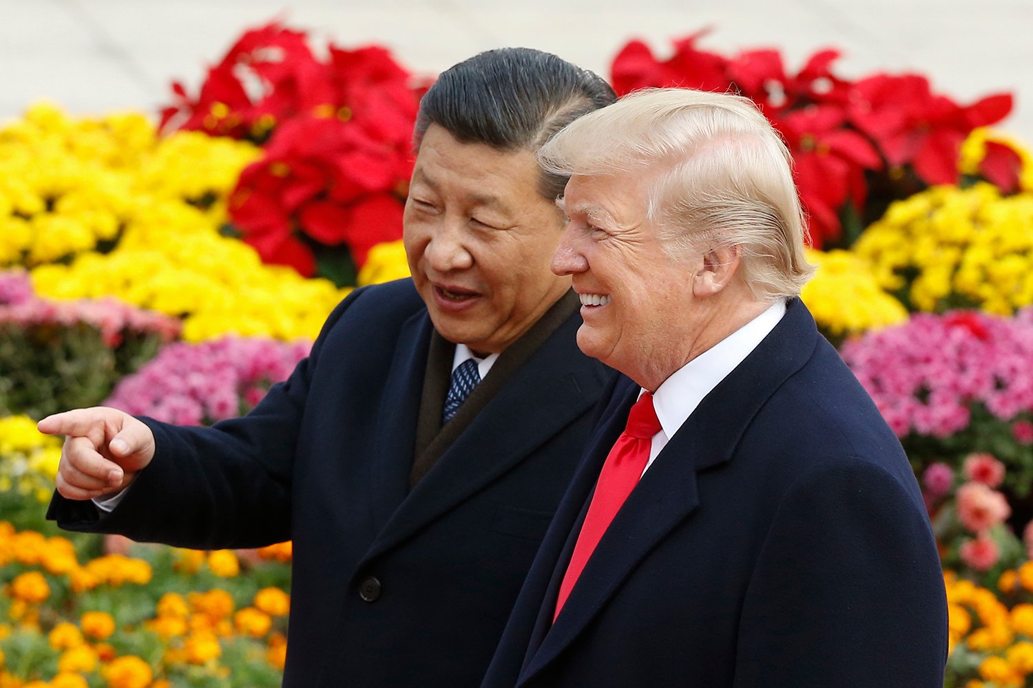 Chinese President Xi Jinping and U.S. President Donald Trump smile together with flowers in the background.