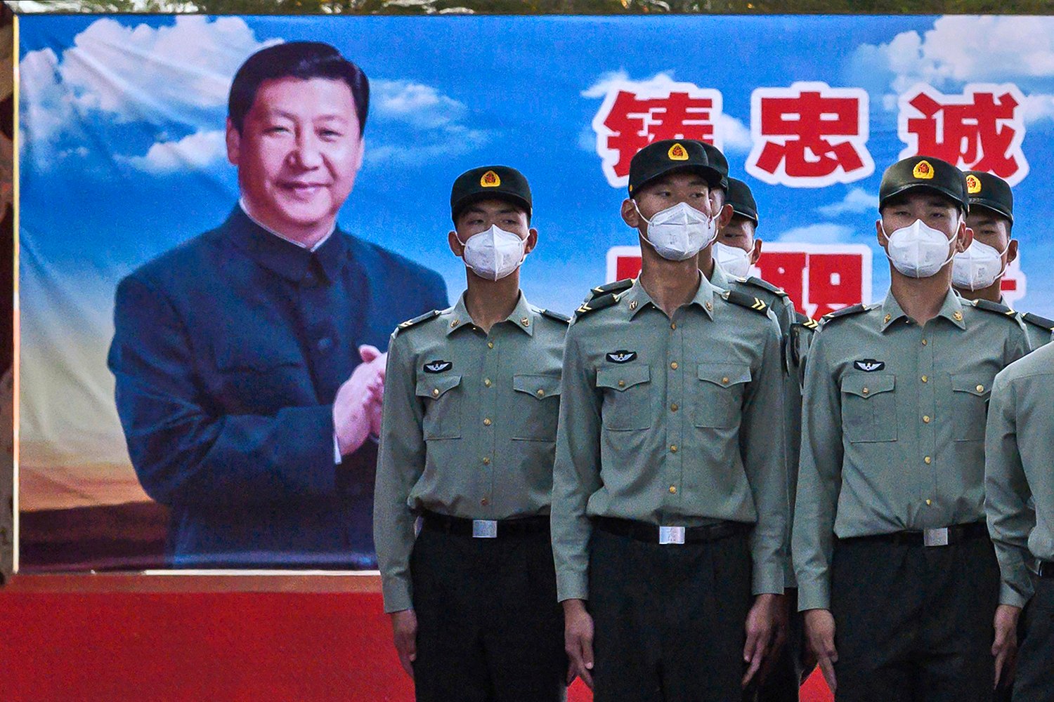 Soldiers wearing protective masks pose in front of a billboard of Xi Jinping.