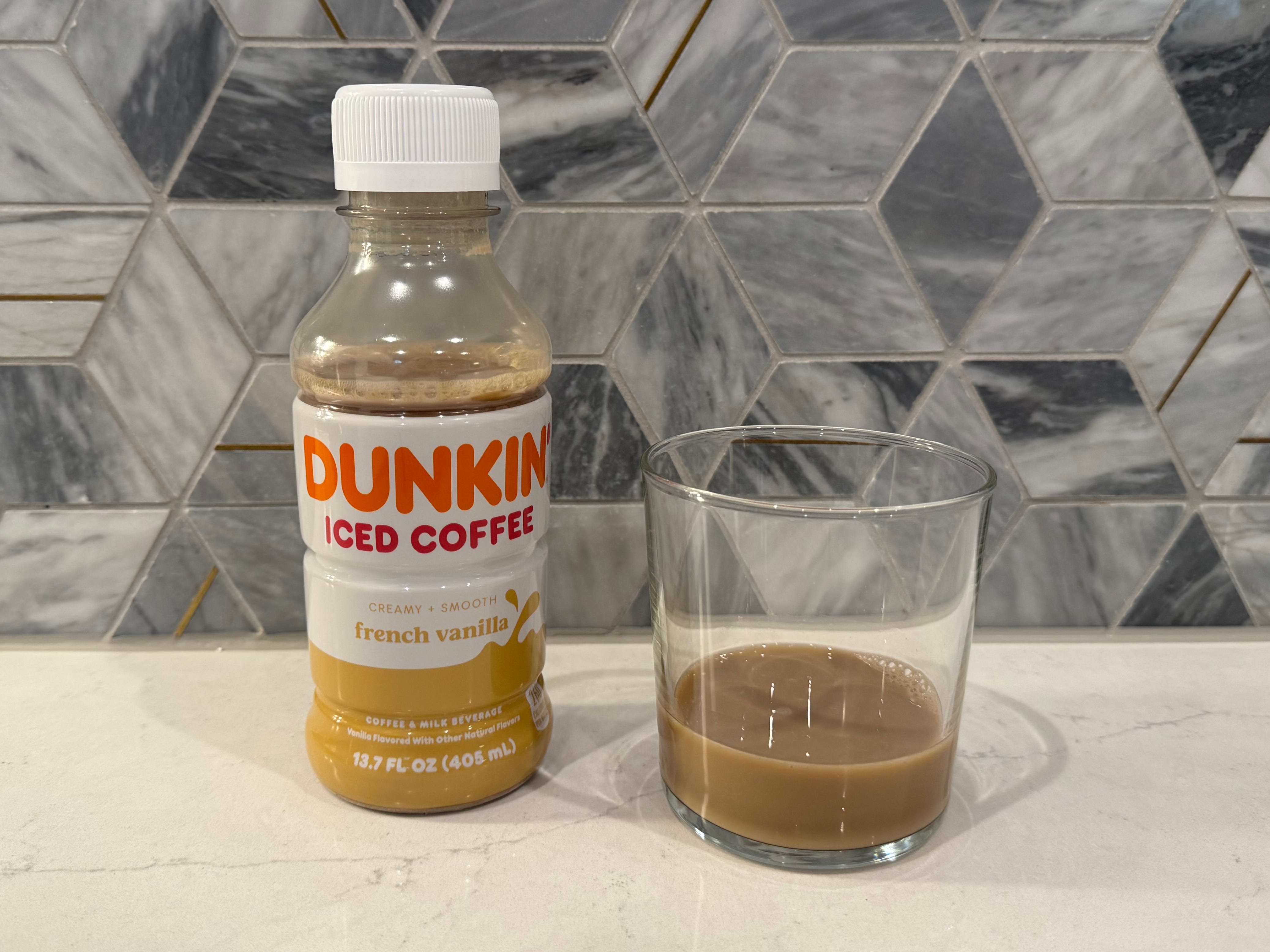 Dunkin vanilla iced coffee bottle next to glass of iced coffee