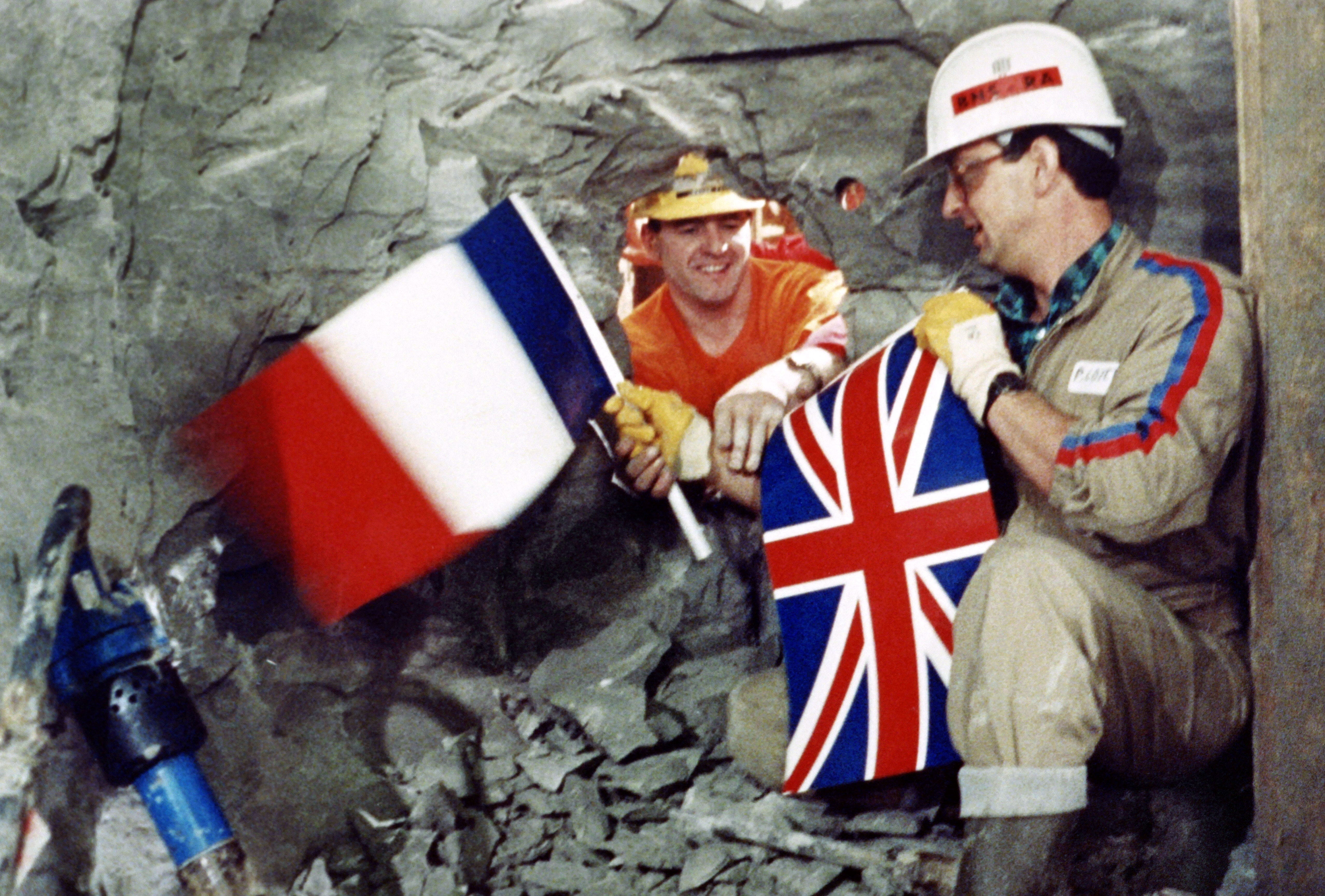 Tunnel workers Philippe Cozette from France (R) and Graham Fagg from England shake hands while holding national flags on December 01, 1990, during the historic breakthrough in the Channel Tunnel.