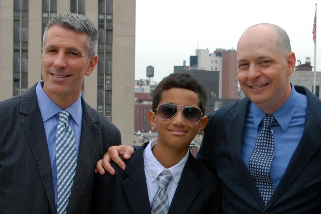 Adolescent Kevin with dads Danny Stewart (left) and Peter Mercurio. All wear suits. 