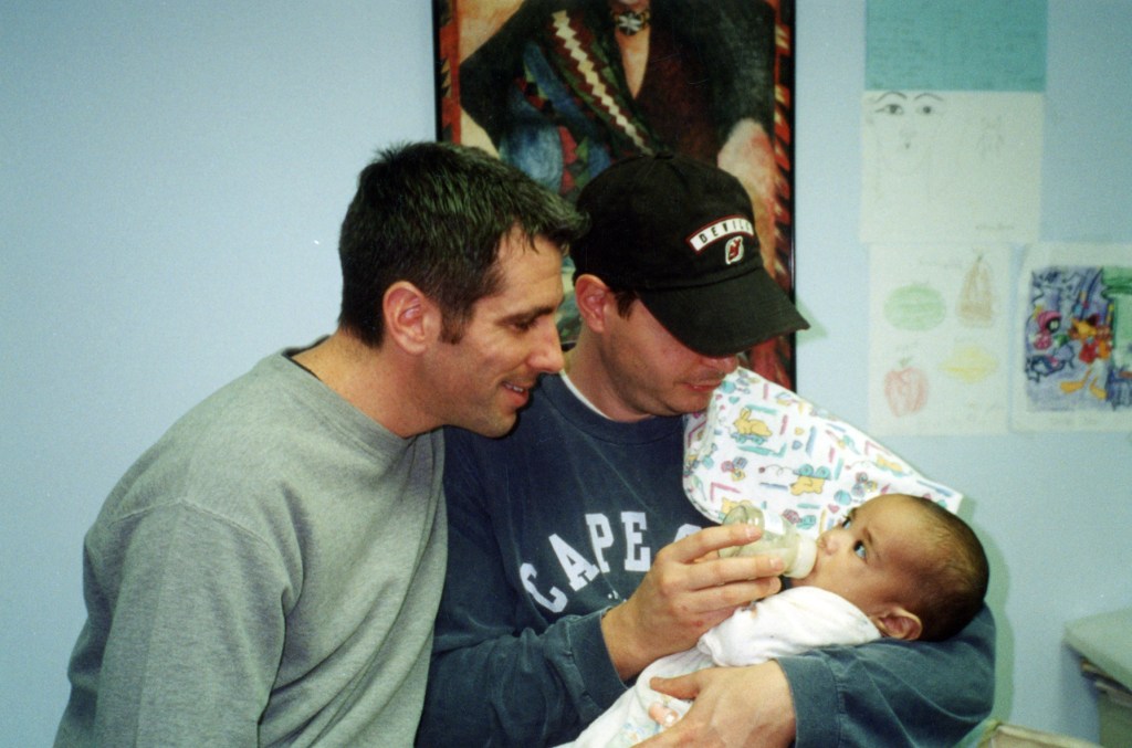 Danny Stewart and Peter Mercurio bottle-feeding a baby.
