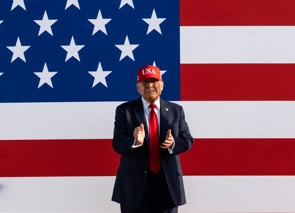 Donald Trump clapping in front of an American flag.