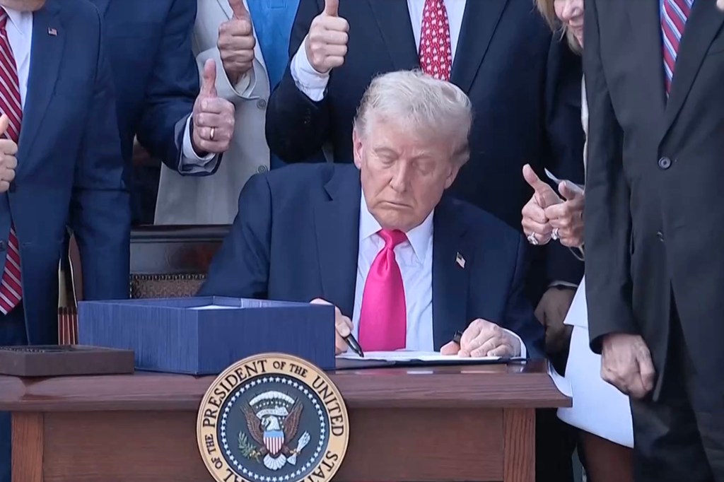 President Trump signing a bill, surrounded by people giving thumbs up.
