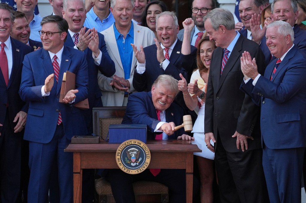 Donald Trump signing legislation, surrounded by applauding people.