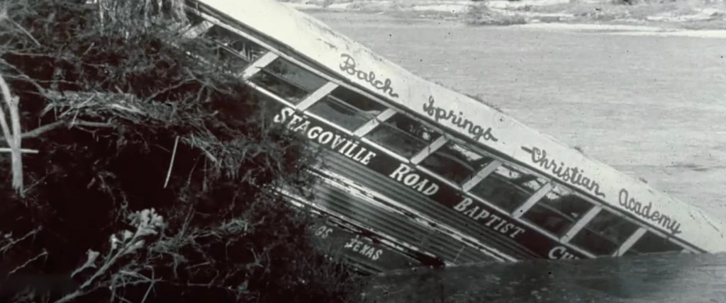 A flooded bus titled into a riverbank.