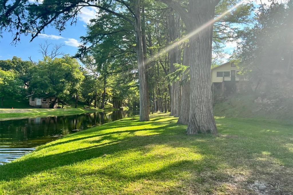 Camp Mystic in Texas: a tranquil scene of a canal, lush green grass, tall trees, and a house.