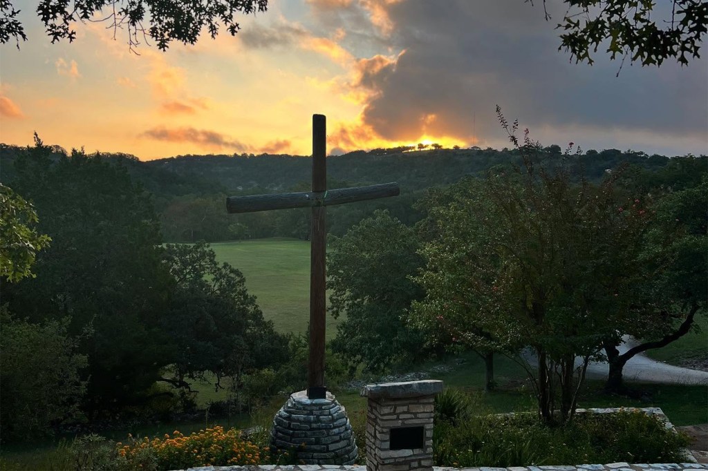 Wooden cross at sunset overlooking a field.
