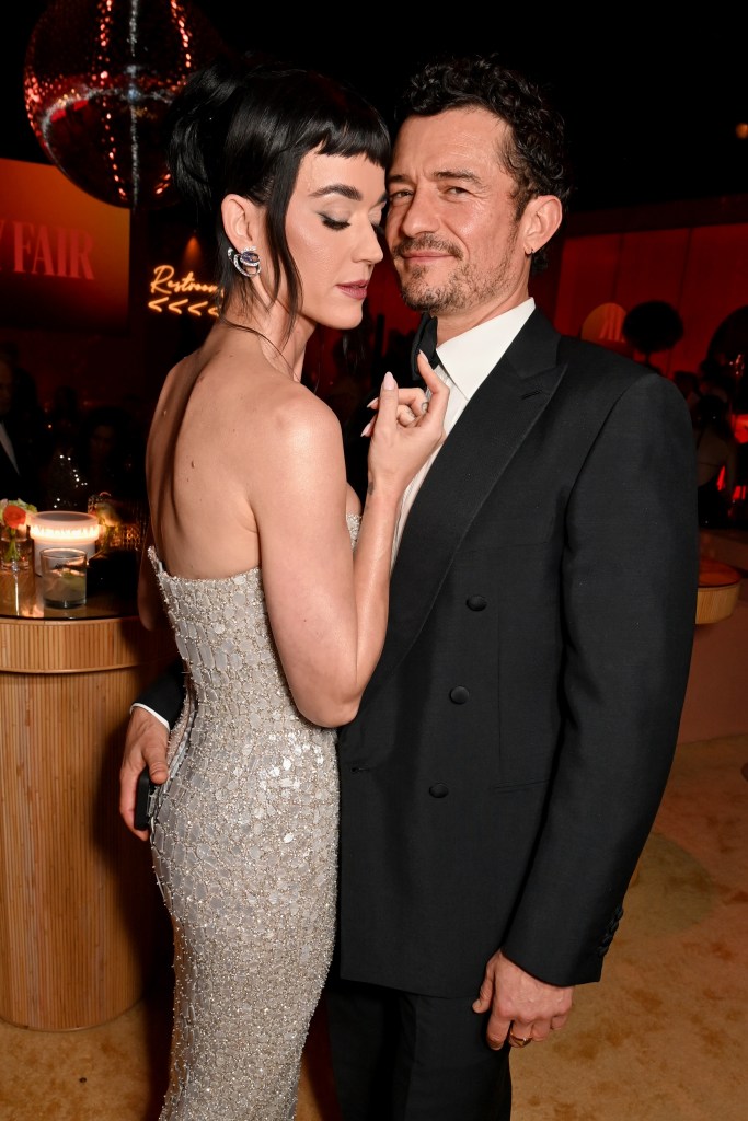 Katy Perry smiling as Orlando Bloom embraces her with a smile. 