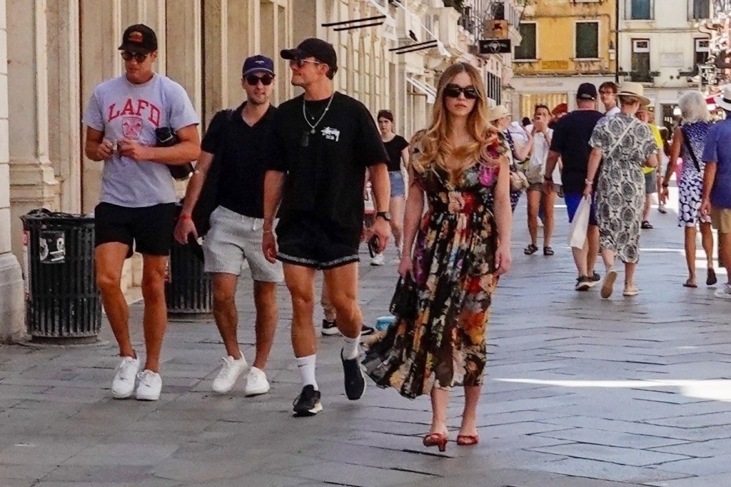 Sydney Sweeney in a floral dress with Orlando Bloom in all black walking beside her in Venice. 