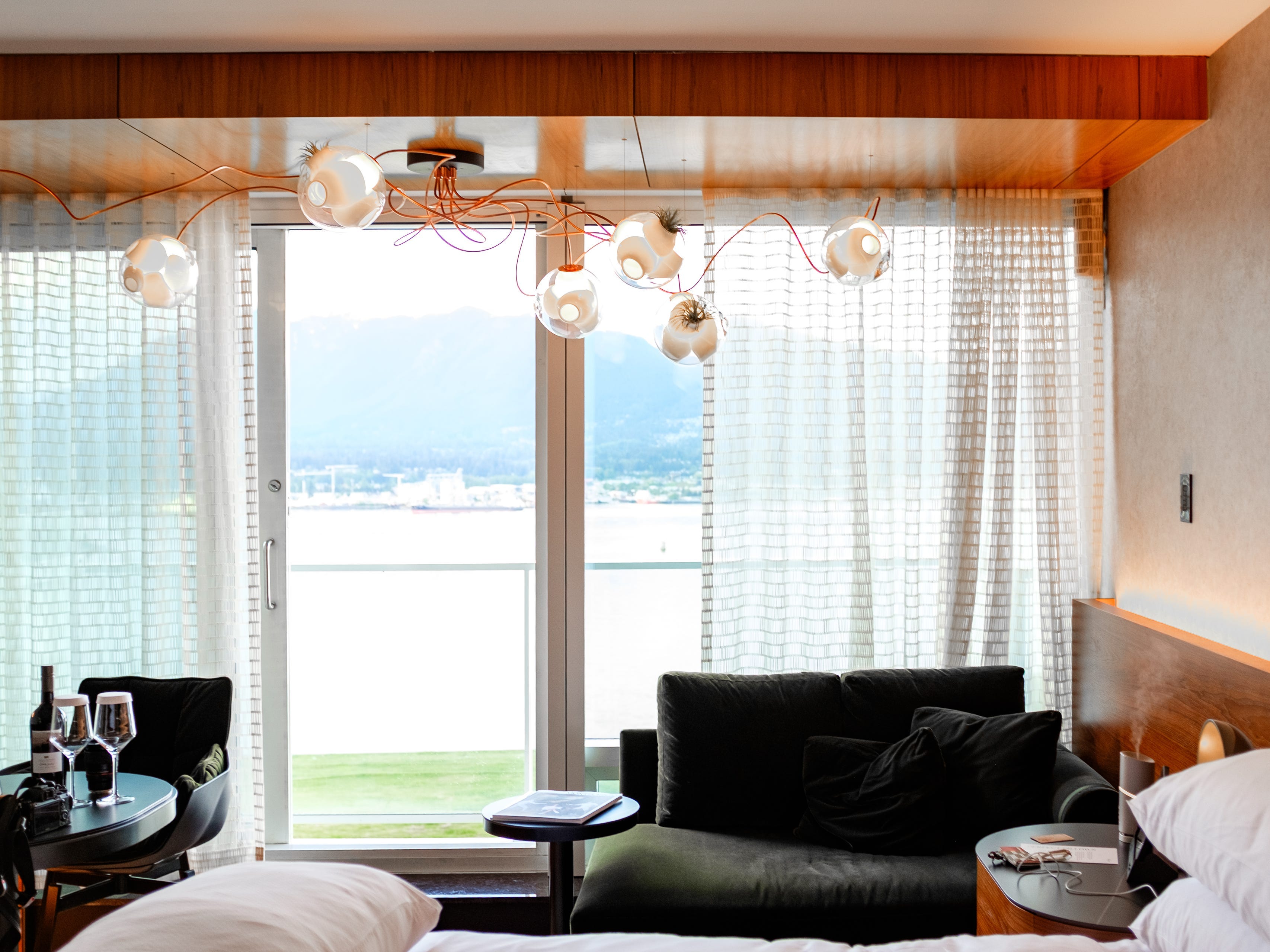 Inside a Fairmont Gold hotel room with an air plant chandelier, seating areas, and a sliding glass door to a balcony at the back of the room