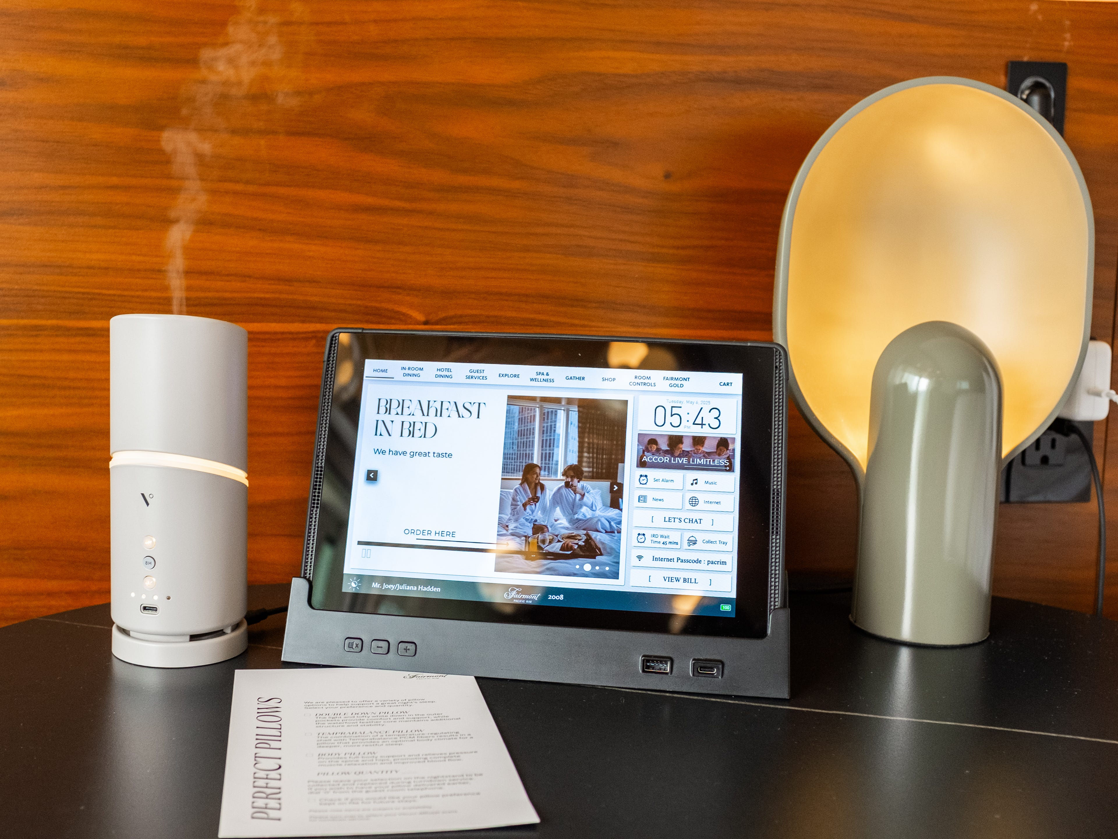 A close-up of a Fairmont Gold hotel room nightstand with an oil diffuser on the left, a tablet in the middle, and a modern lamp on the right