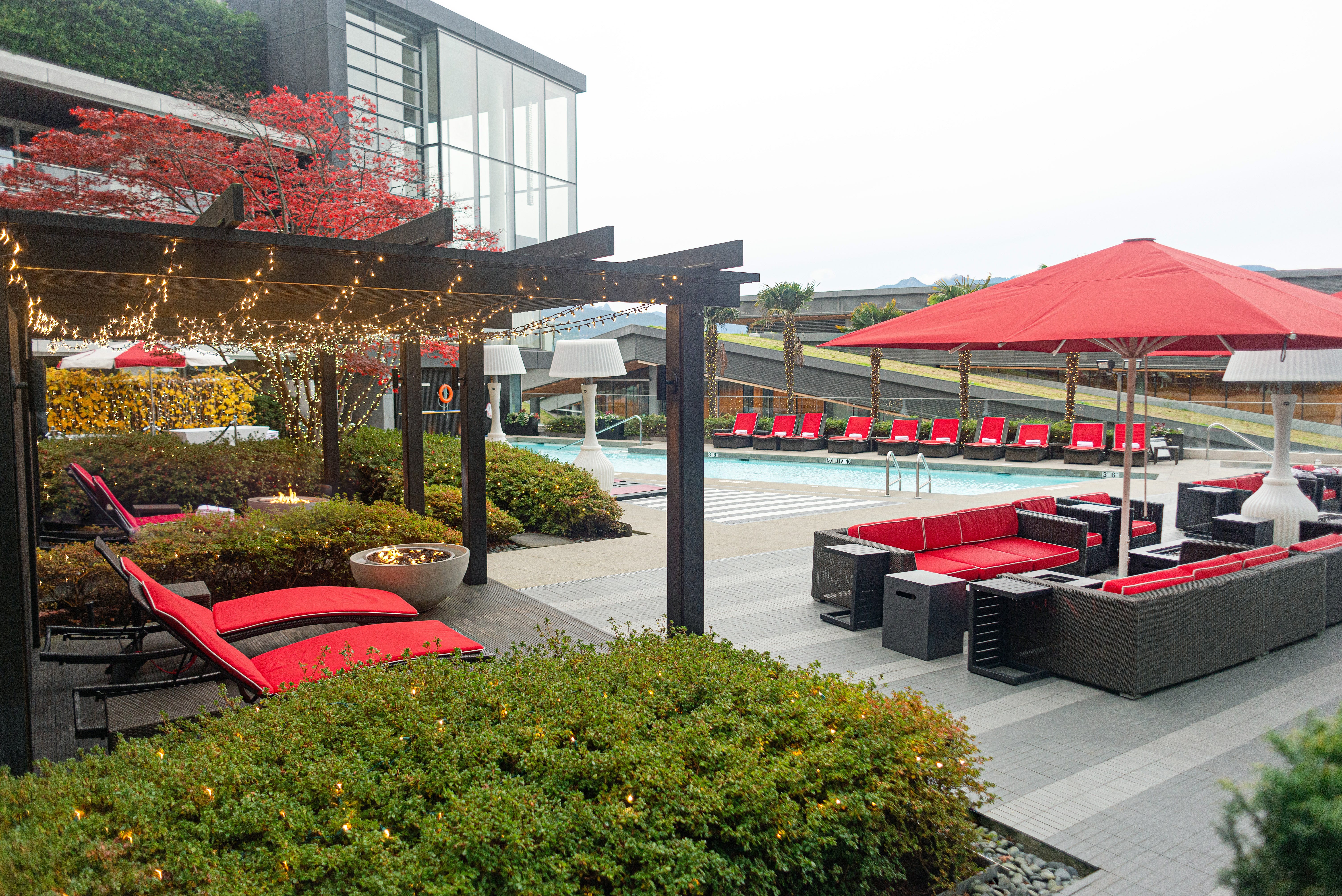 A rooftop hotel pool with red seating and umbrellas at Fairmont Pacific Rim