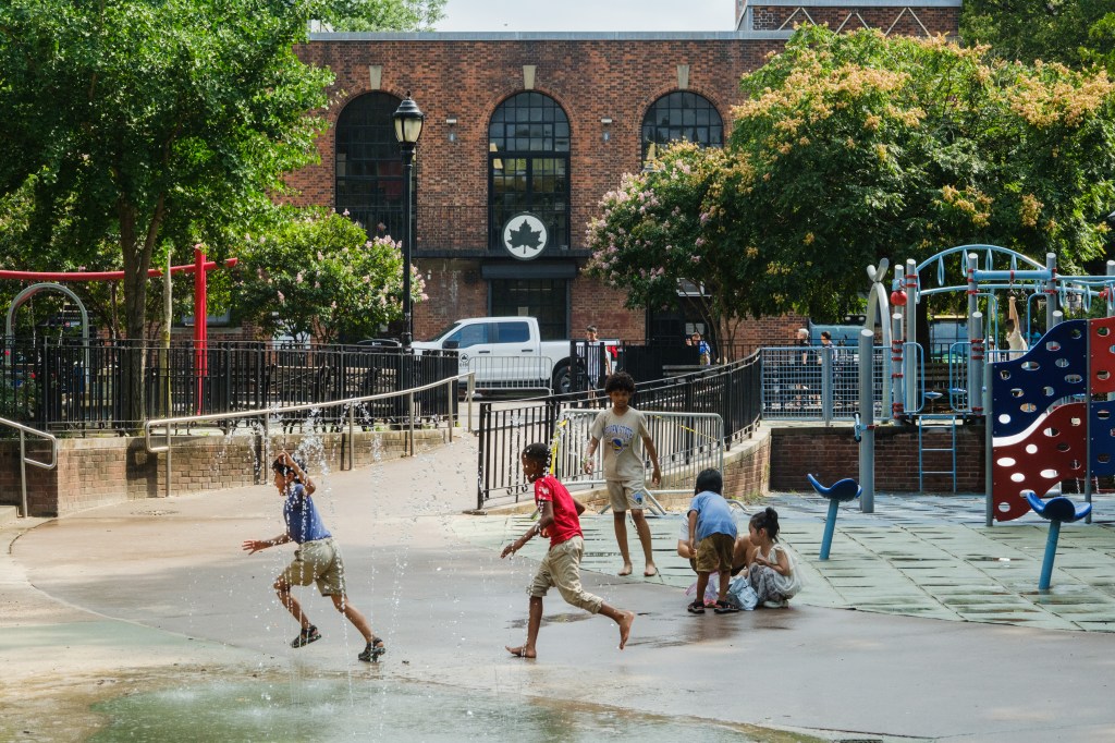 Children playing in a spray park near a playground.
