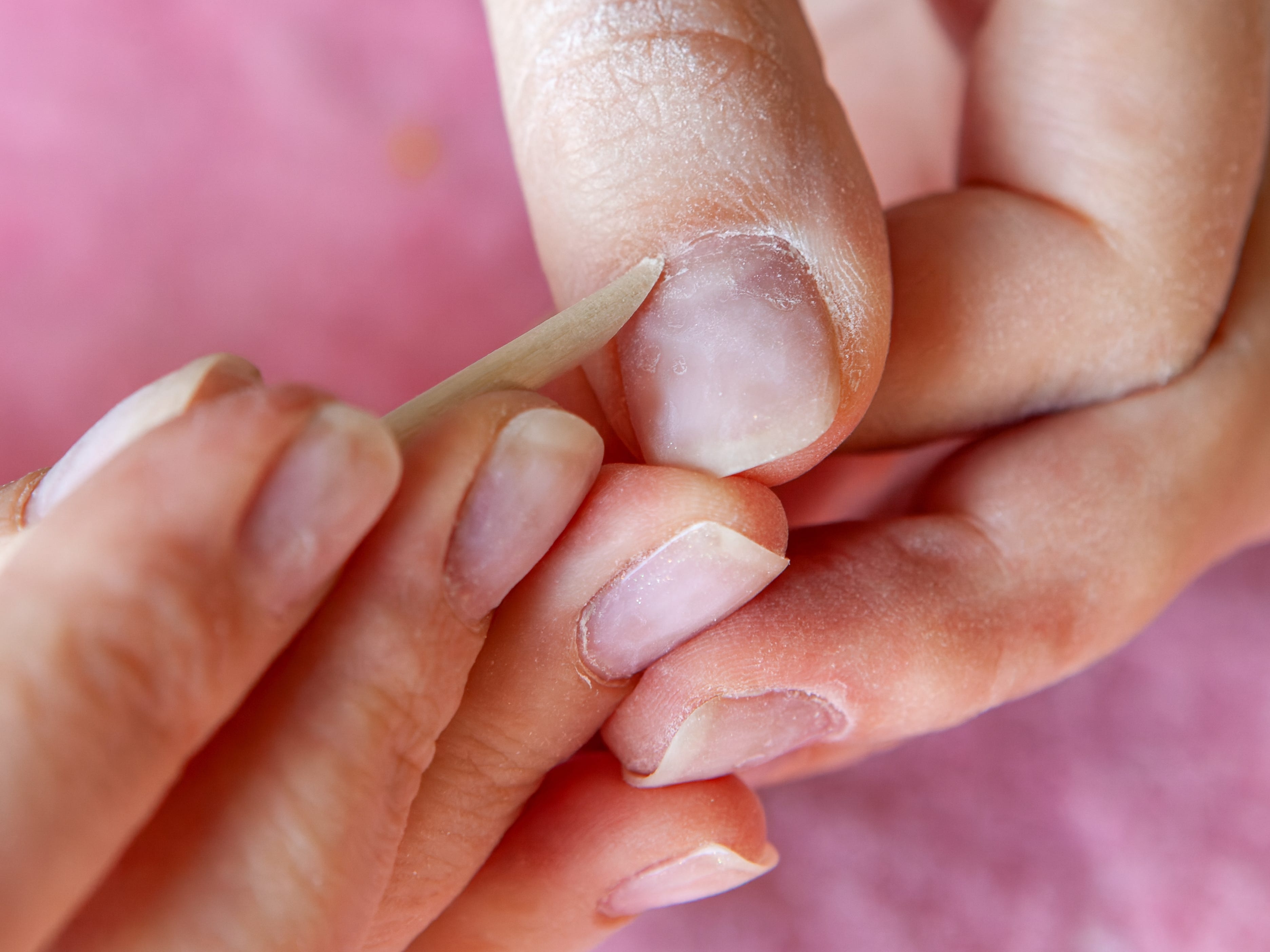 A close-up of fingernails as someone uses a wooden cuticle stick to push back their cuticles.