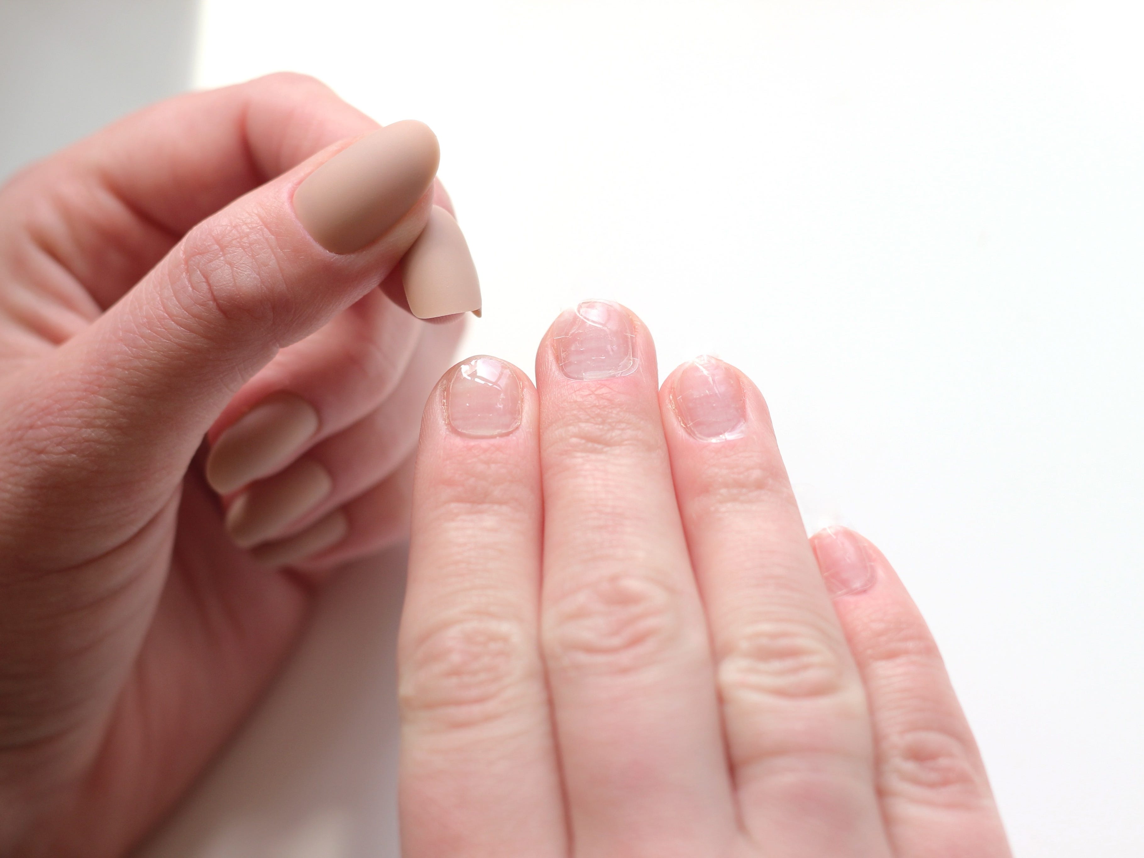 A close-up of hands as the left hand presses a fake nail onto the right hand's natural nail, which has nail glue applied.