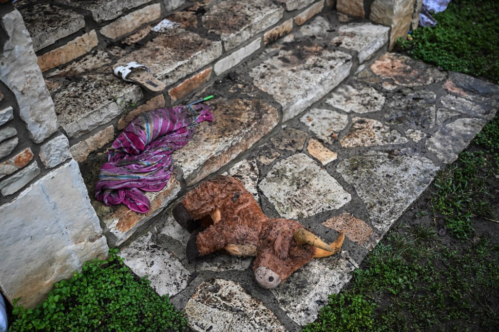 Muddy stuffed bull and discarded clothing near stone steps after a flood.