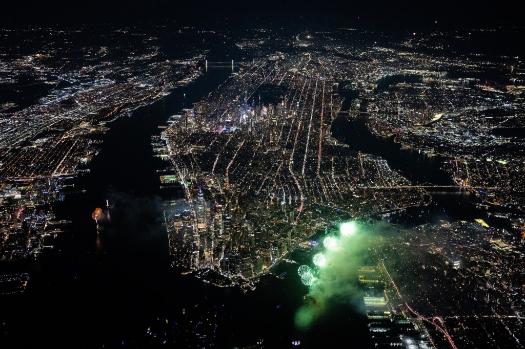 Aerial view of New York City at night with fireworks over the East River.