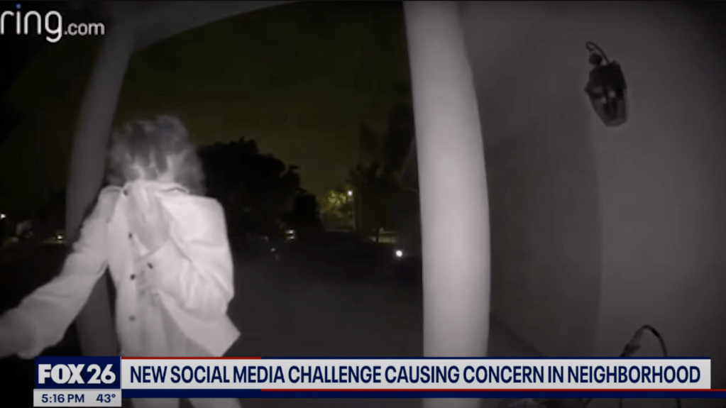 Nighttime Ring security camera footage of a person in a white jacket near a house.