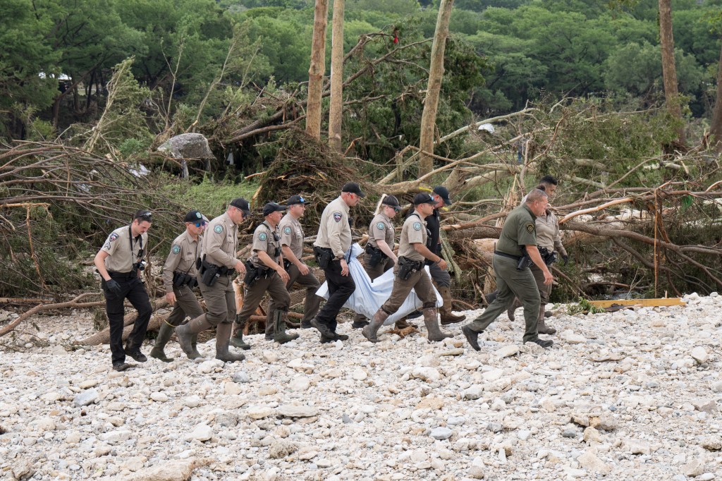 Texas game wardens and law enforcement officers carry a body from a flood-damaged area.