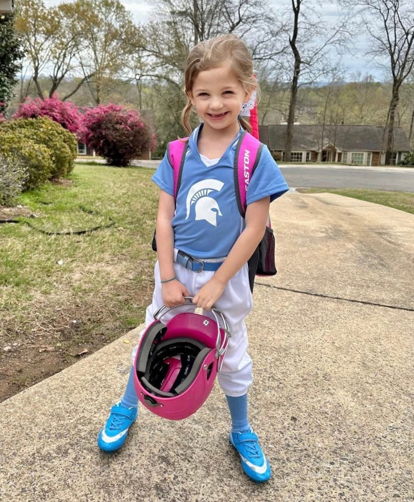 Girl in softball uniform holding helmet.