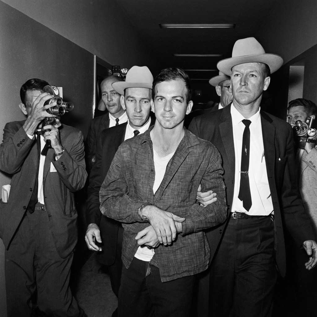 Lee Harvey Oswald in handcuffs, escorted by police officers.