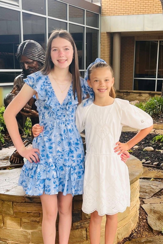 Two girls in dresses posing together near a statue.