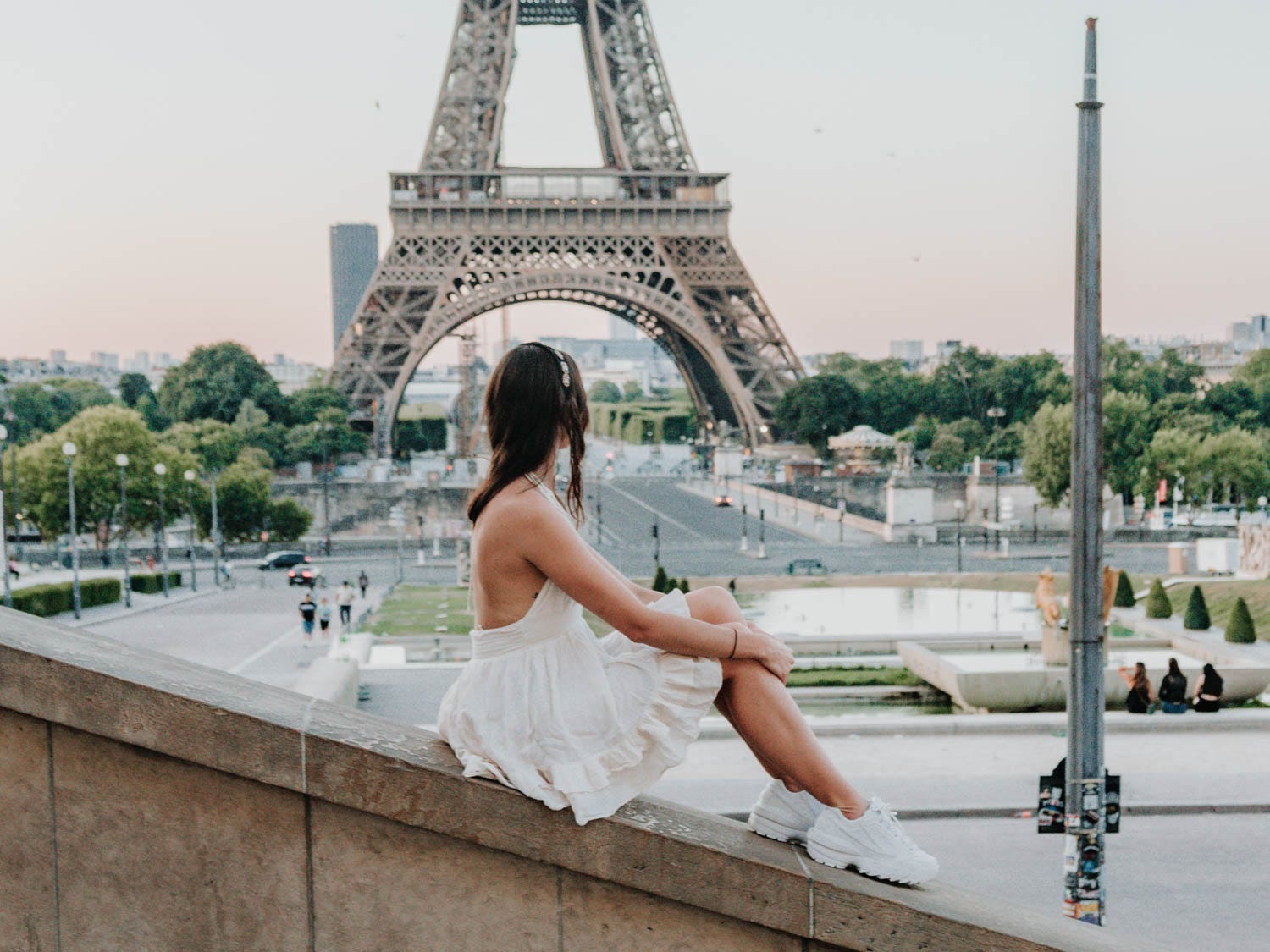 The author wearing a white dress and sitting on a bridge, staring at the Eiffel Tower.