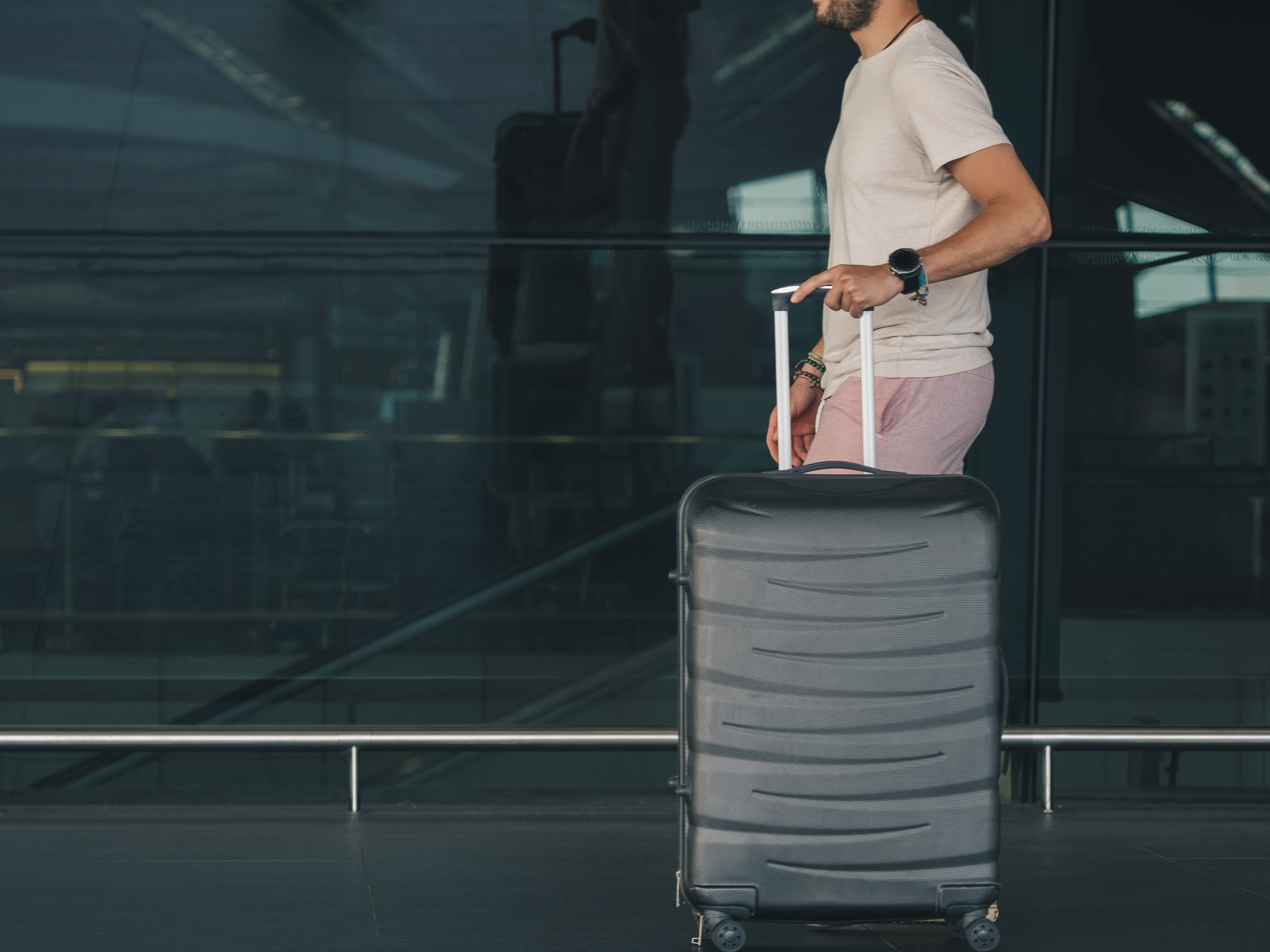 A man walks through the airport while rolling a black suitcase by his side.