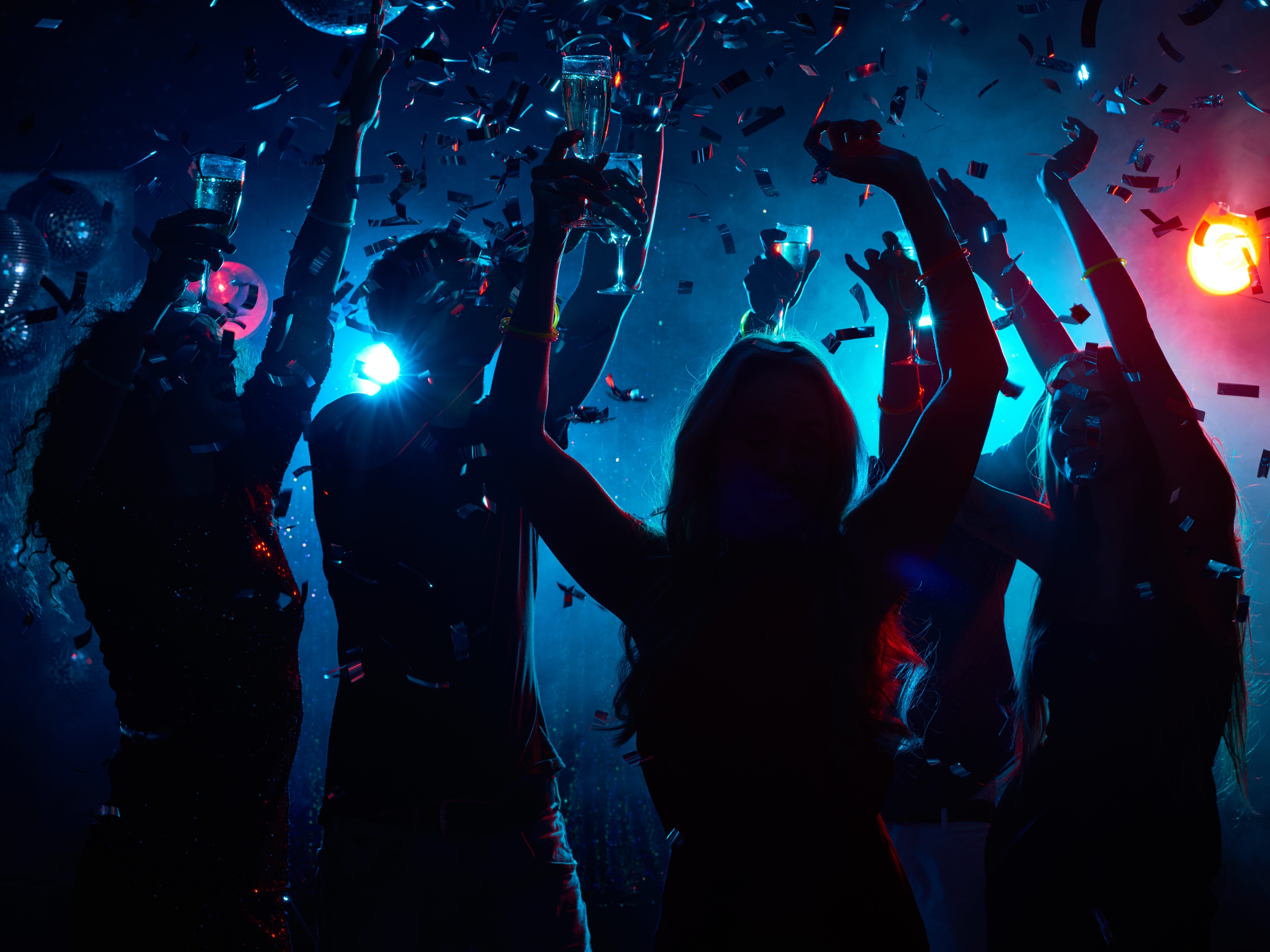 Silouettes of people dancing at a party, holding glasses as confetti falls around them.