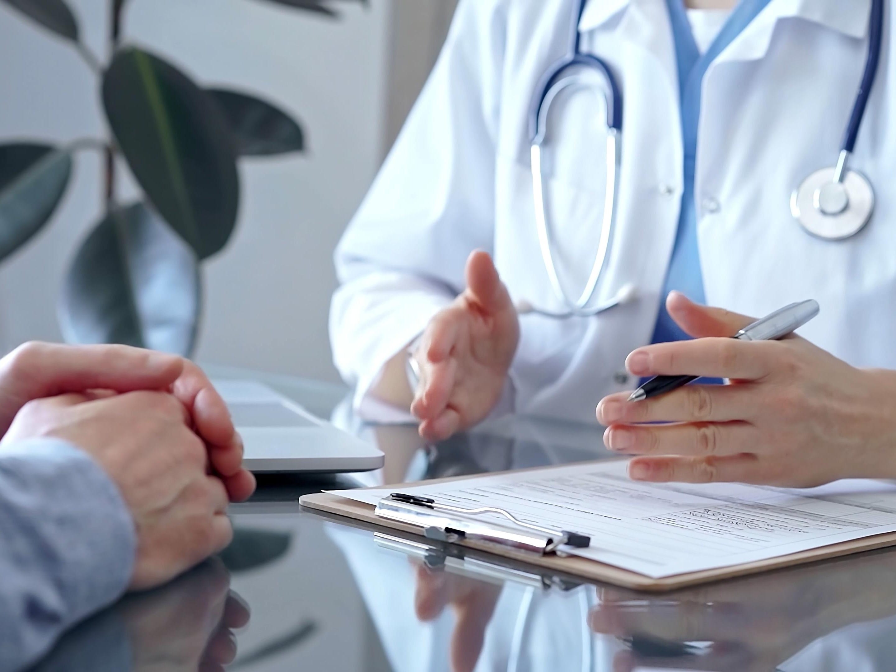 Close-up of a doctor's hands holding a pen over a clipboard on a table, consulting with a patient.