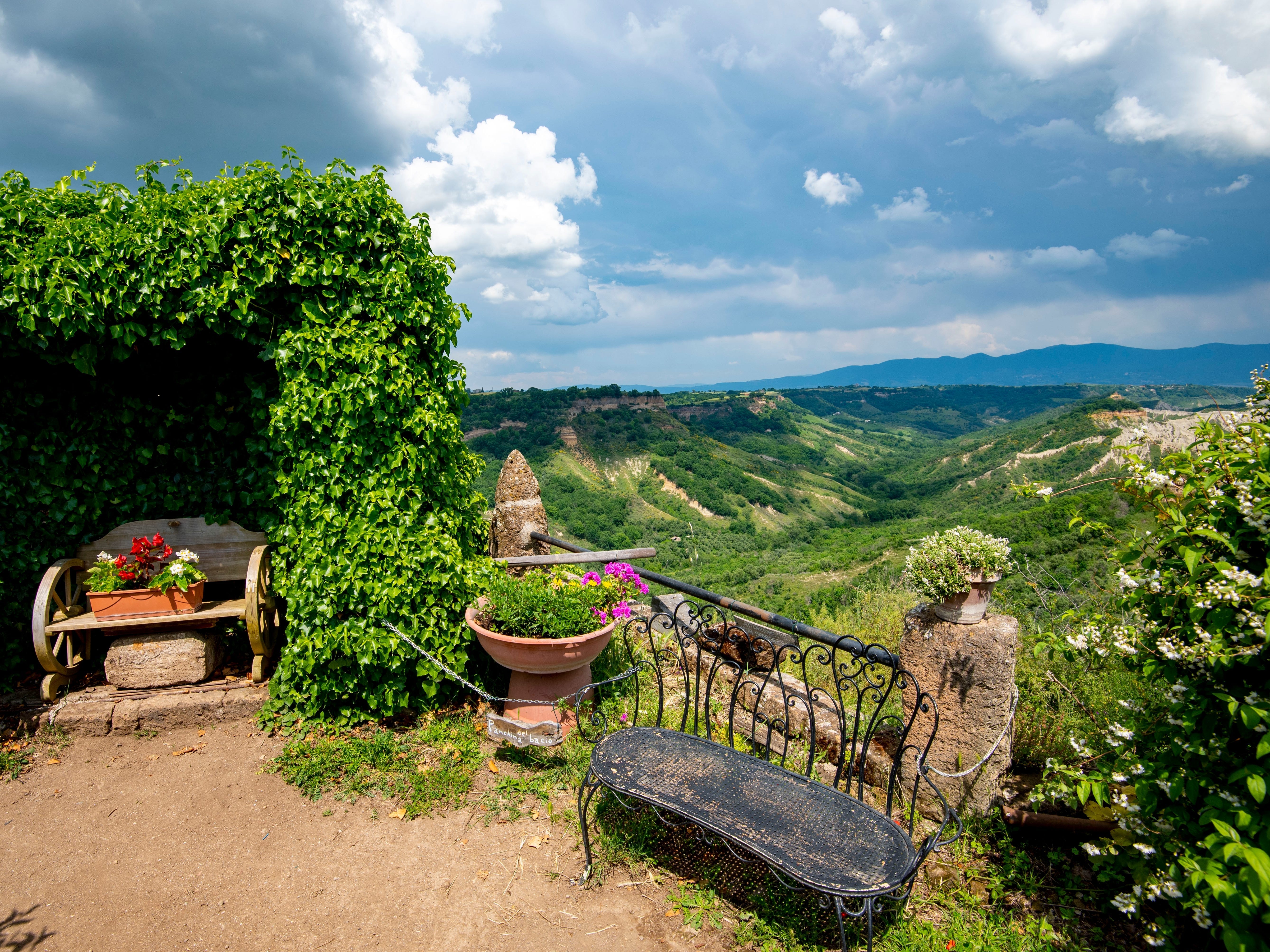 A garden with benches, flowers, and ivy, overlooking beautiful greenery-covered mountains.