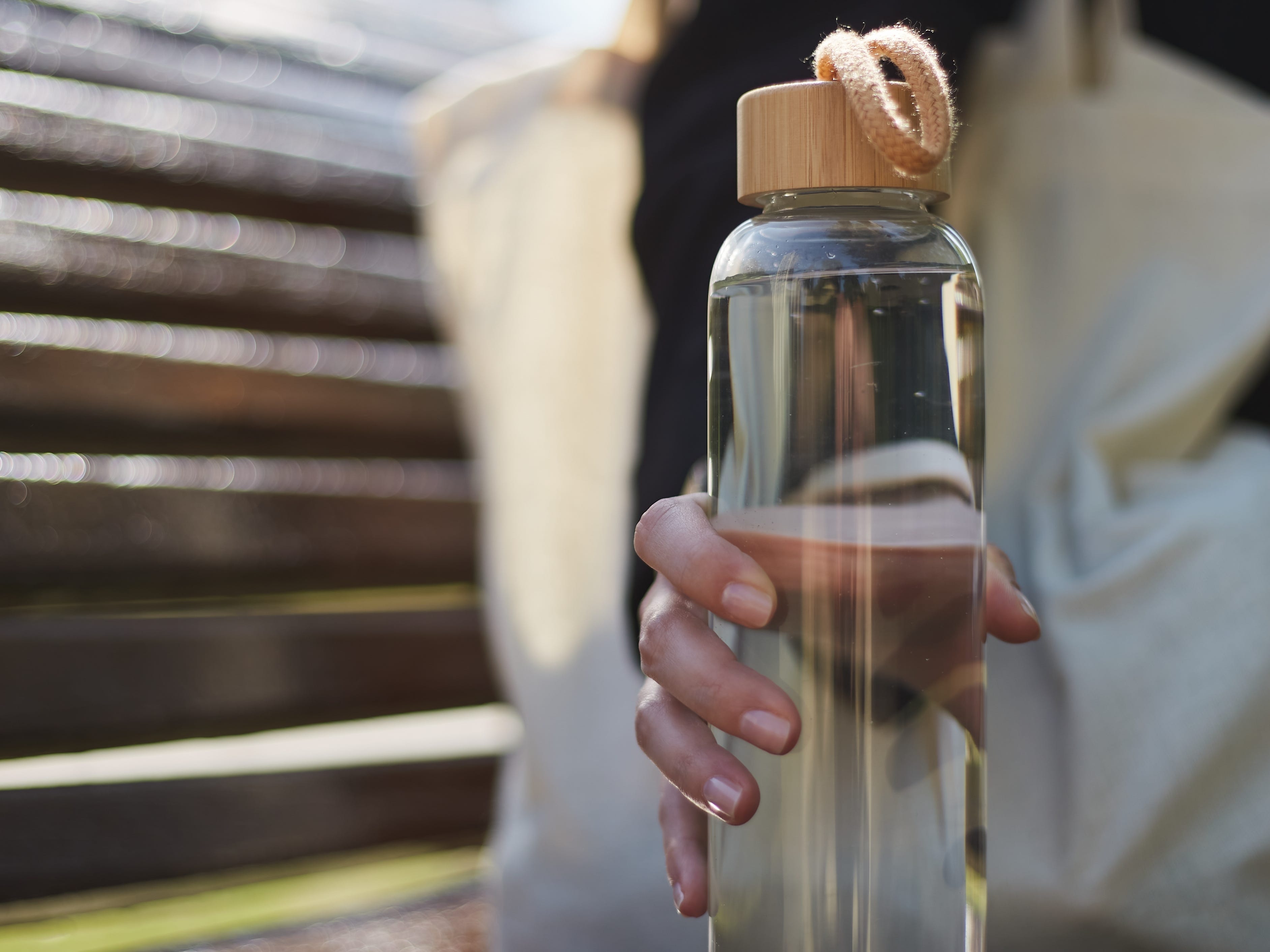 person sitting on a bench with a tote bag and a reusable glass water bottle