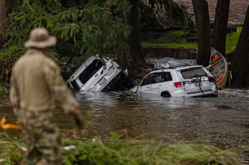 Vehicles sit submerged as a search and rescue worker looks through debris for any survivors or remains of people swept up in the flash flooding on July 6, 2025 in Hunt, Texas that left at last 82 people dead and dozens still missing.